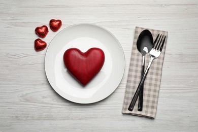 Beautiful place setting with dishware, sweets and decorative heart for romantic dinner on white wooden table, flat lay