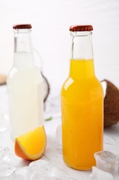 Photo of Tasty kombucha in glass bottles, orange and ice on white table
