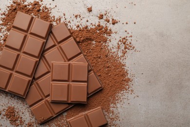 Photo of Delicious milk chocolate and cocoa powder on light grey table, flat lay. Space for text