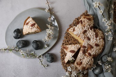 Delicious cut Italian Easter dove cake (traditional Colomba di Pasqua), painted eggs and flowering branches on grey textured table, flat lay