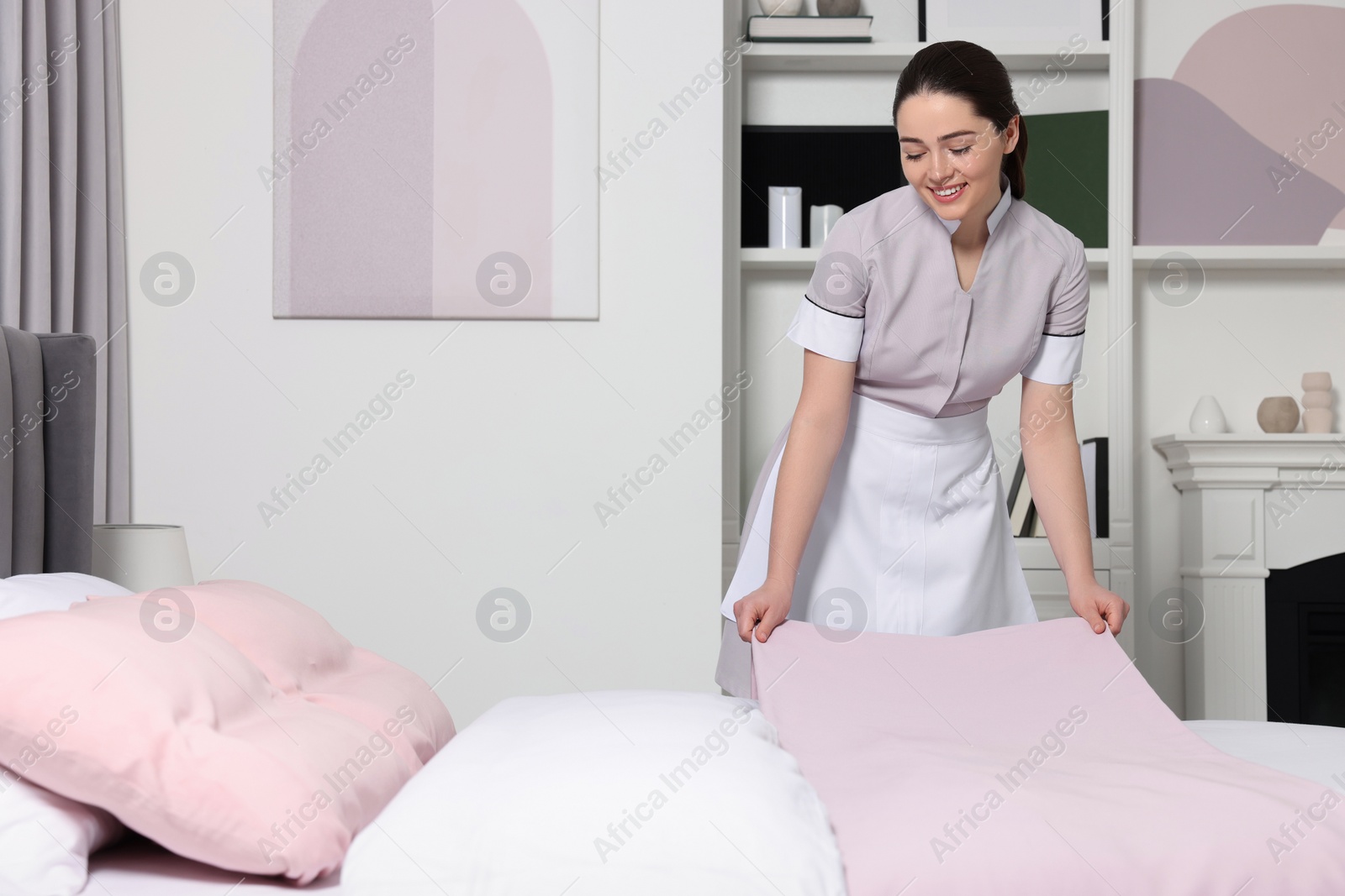 Photo of Young maid making bed in hotel room. Space for text