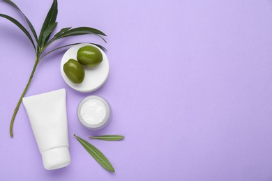 Photo of Tube and jar of cream with olive essential oil on violet background, flat lay. Space for text