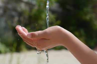 Photo of Pouring water into kid`s hand outdoors, closeup