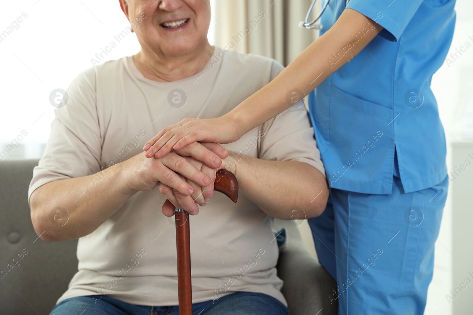 Photo of Nurse assisting elderly man with cane indoors, closeup
