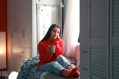 Photo of Young woman with cup of drink on couch at home. Winter season
