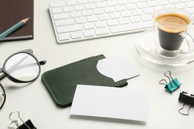 Photo of Leather business card holder with blank cards, glasses, coffee, keyboard and stationery on white table