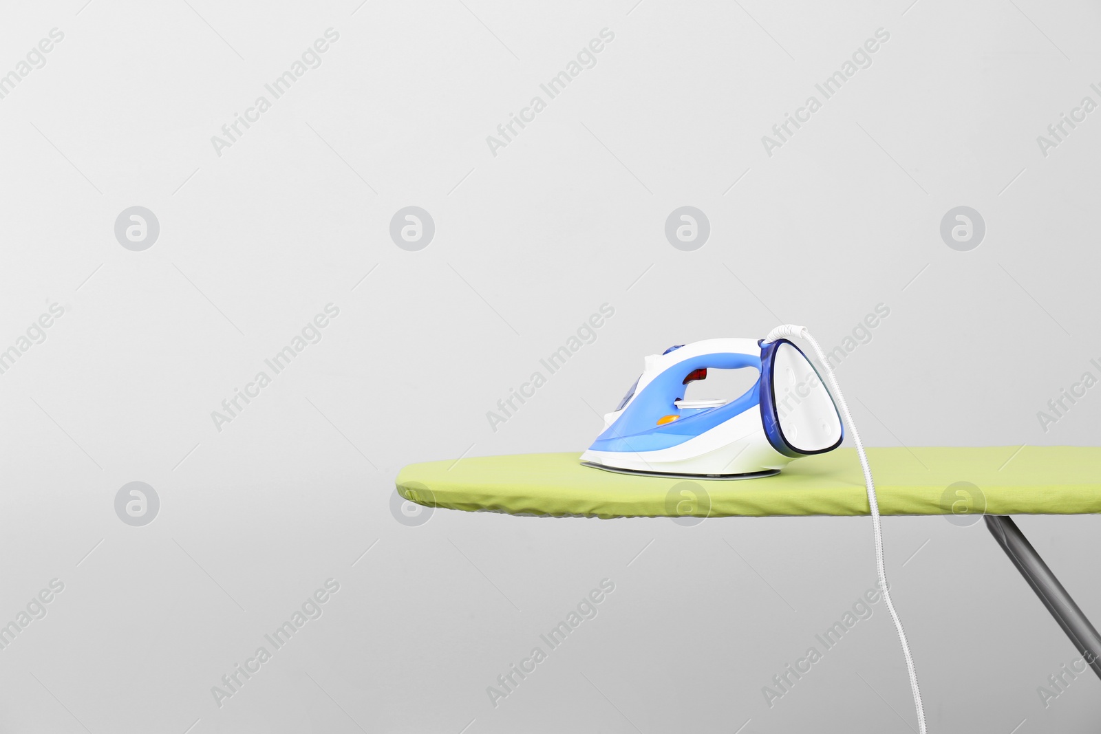 Photo of Modern electric iron on board against light background, space for text