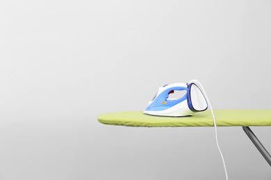 Photo of Modern electric iron on board against light background, space for text