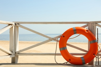 Photo of Orange life buoy near wooden railing on beach.  Emergency rescue equipment