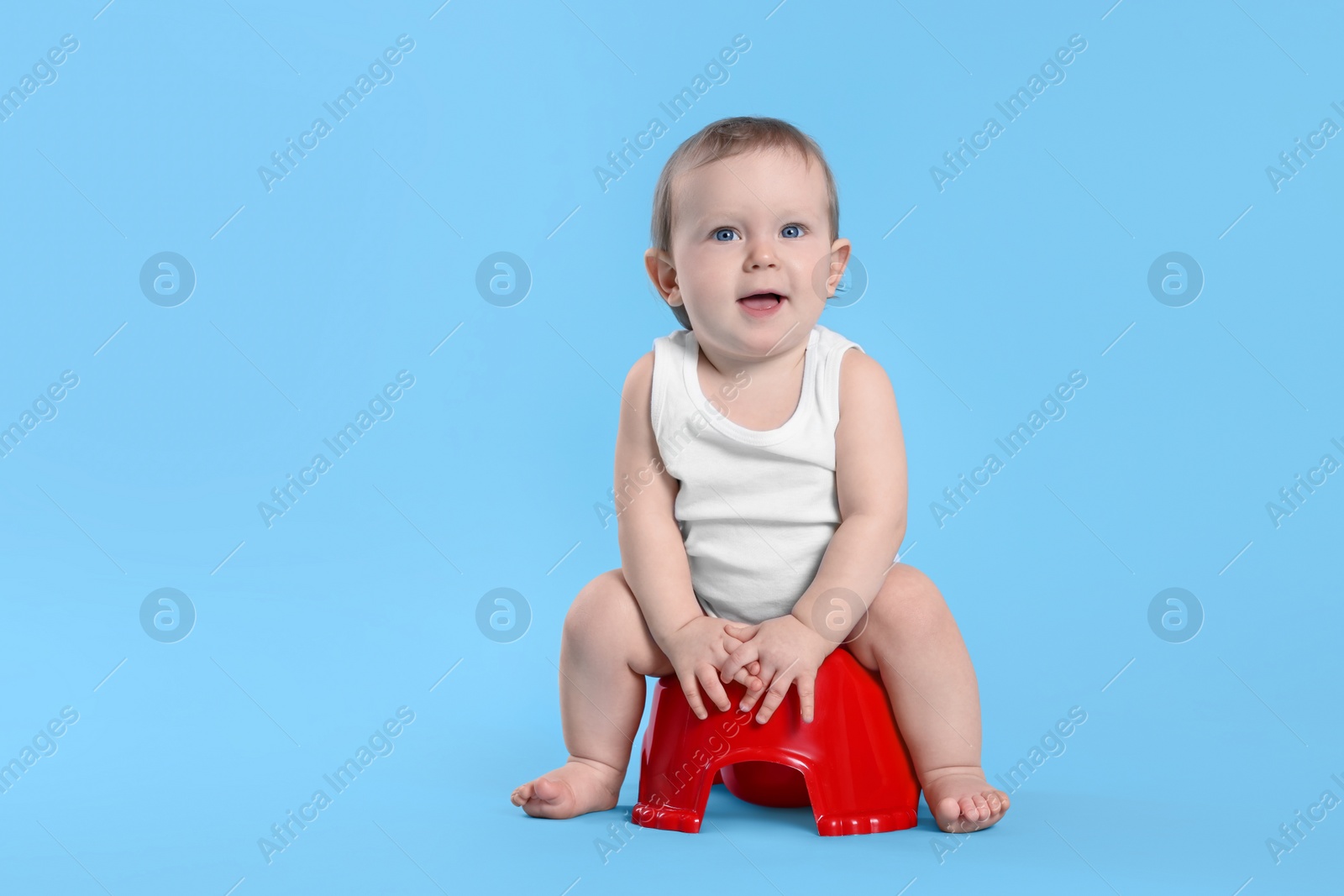 Photo of Little child sitting on baby potty against light blue background. Space for text