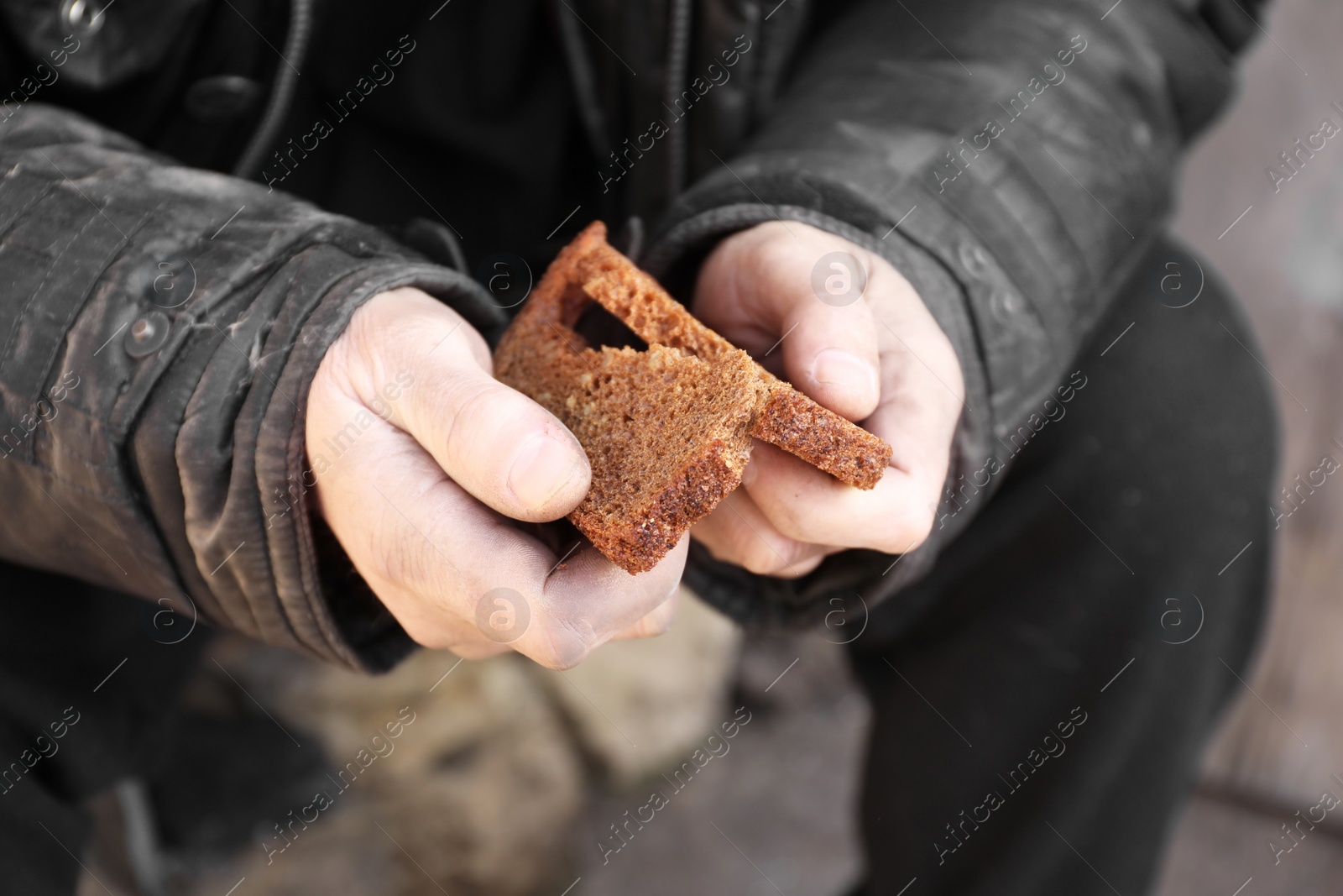 Photo of Poor homeless man holding piece of bread outdoors, closeup