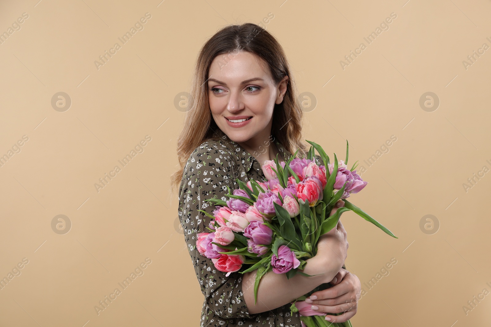 Photo of Happy young woman holding bouquet of beautiful tulips on beige background