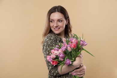 Photo of Happy young woman holding bouquet of beautiful tulips on beige background