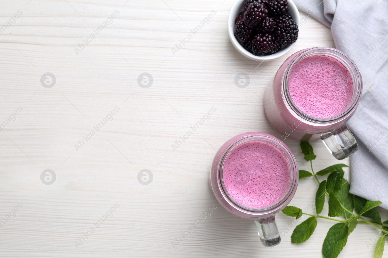 Photo of Mason jars of blackberry smoothie with mint and berries on white wooden table, flat lay. Space for text