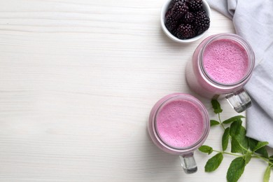 Mason jars of blackberry smoothie with mint and berries on white wooden table, flat lay. Space for text