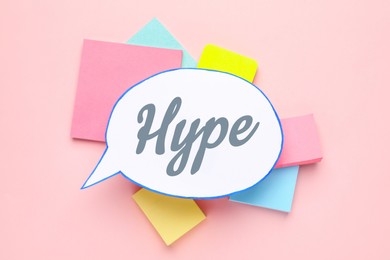 Image of Paper speech bubble with word Hype and notes on pink background, flat lay