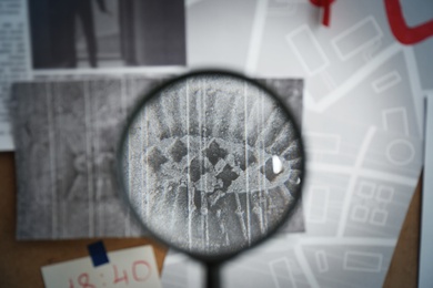 Photo of Looking through magnifying glass at photo of footprint on detective board, closeup
