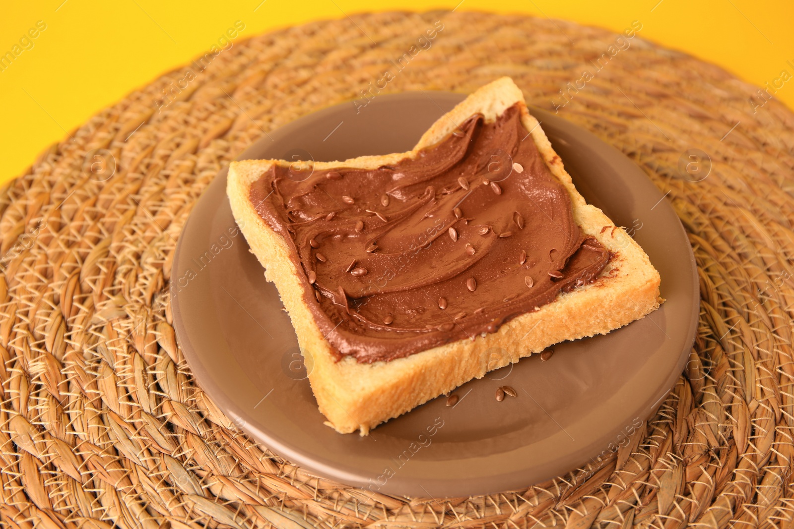 Photo of Tasty toast with chocolate paste and flax seeds on yellow background, closeup view