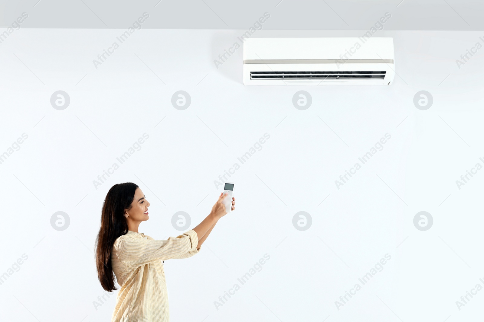 Photo of Young woman turning on air conditioner against white background