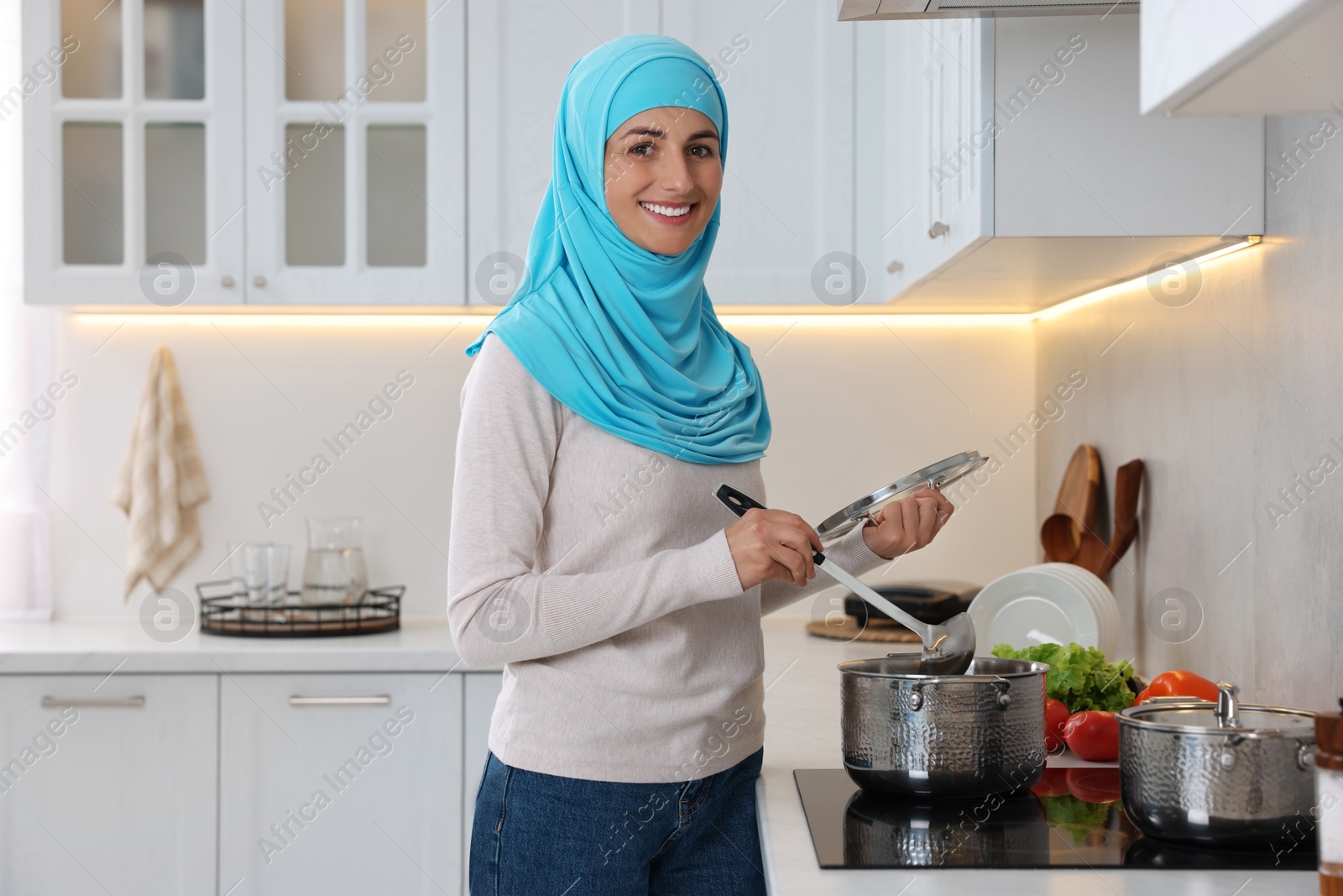 Photo of Muslim woman cooking dish in saucepan on cooktop indoors