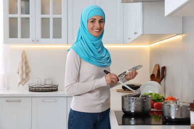 Muslim woman cooking dish in saucepan on cooktop indoors