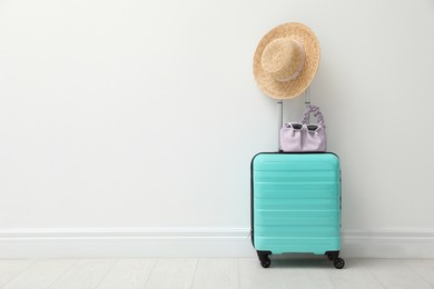 Photo of Packed suitcase and summer accessories near white wall indoors. Space for text