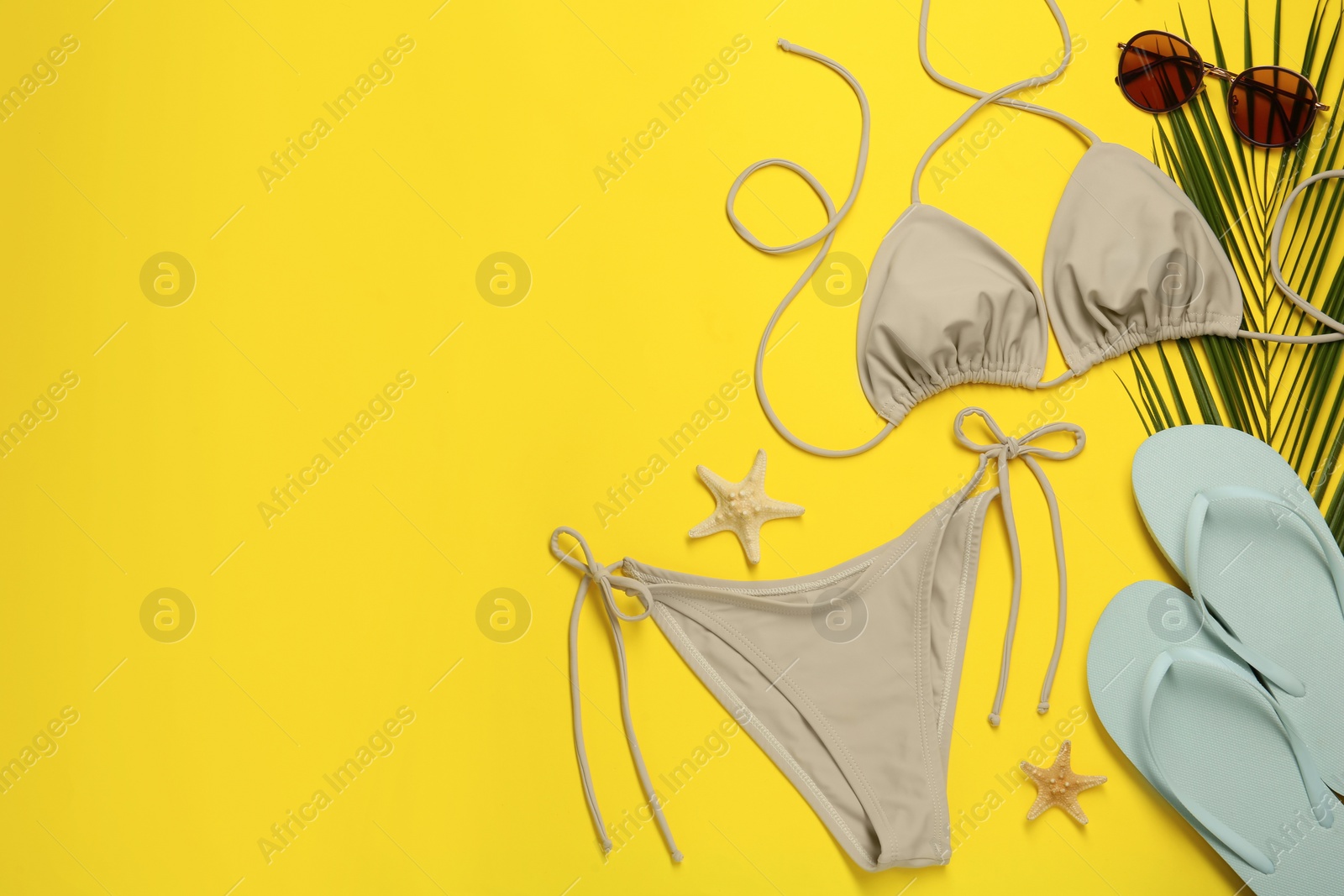 Photo of Stylish beige bikini and beach accessories on yellow background, flat lay. Space for text