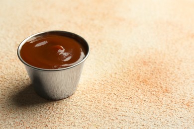 Photo of Tasty barbeque sauce in bowl on beige textured table, closeup. Space for text