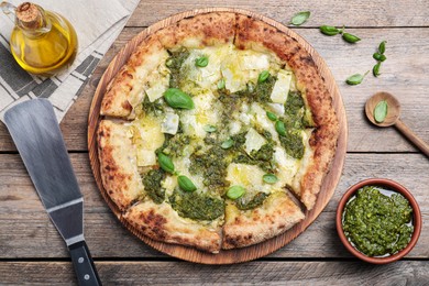 Photo of Delicious pizza with pesto, cheese and basil served on wooden table, flat lay