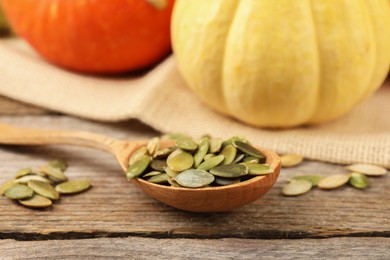 Photo of Spoon with peeled seeds and fresh pumpkins on wooden table, closeup