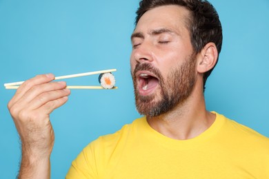 Handsome man eating sushi roll with chopsticks on light blue background