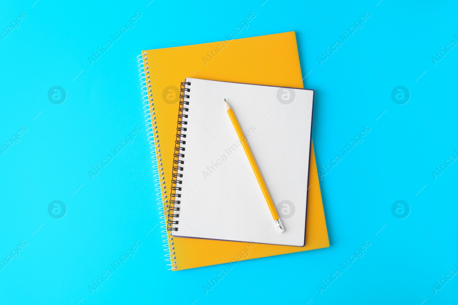 Photo of Notebooks with pencil on light blue background, top view