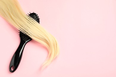 Photo of Stylish brush with blonde hair strand on pink background, top view. Space for text