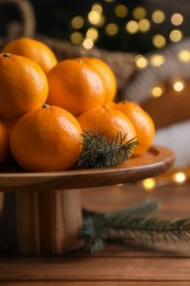 Photo of Stand with delicious ripe tangerines and fir twigs on wooden table