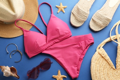 Photo of Beautiful pink bikini and beach accessories on blue  background, flat lay