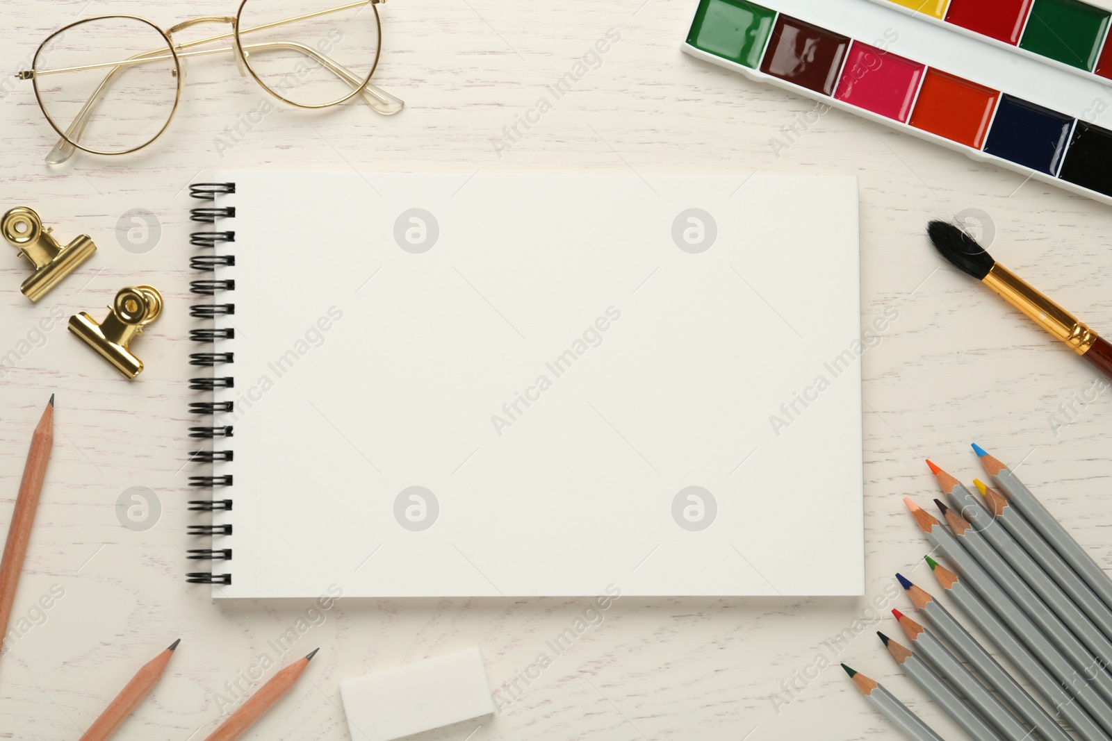 Photo of Flat lay composition with blank sketchbook on white wooden table. Space for text