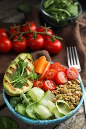Photo of Delicious lentil bowl with avocado, tomatoes, carrot and cucumber on wooden table