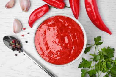 Bowl of hot chili sauce with ingredients on table, flat lay