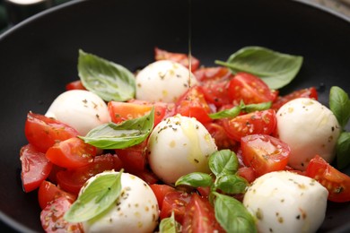 Photo of Pouring oil onto tasty salad Caprese with tomatoes, mozzarella balls and basil, closeup