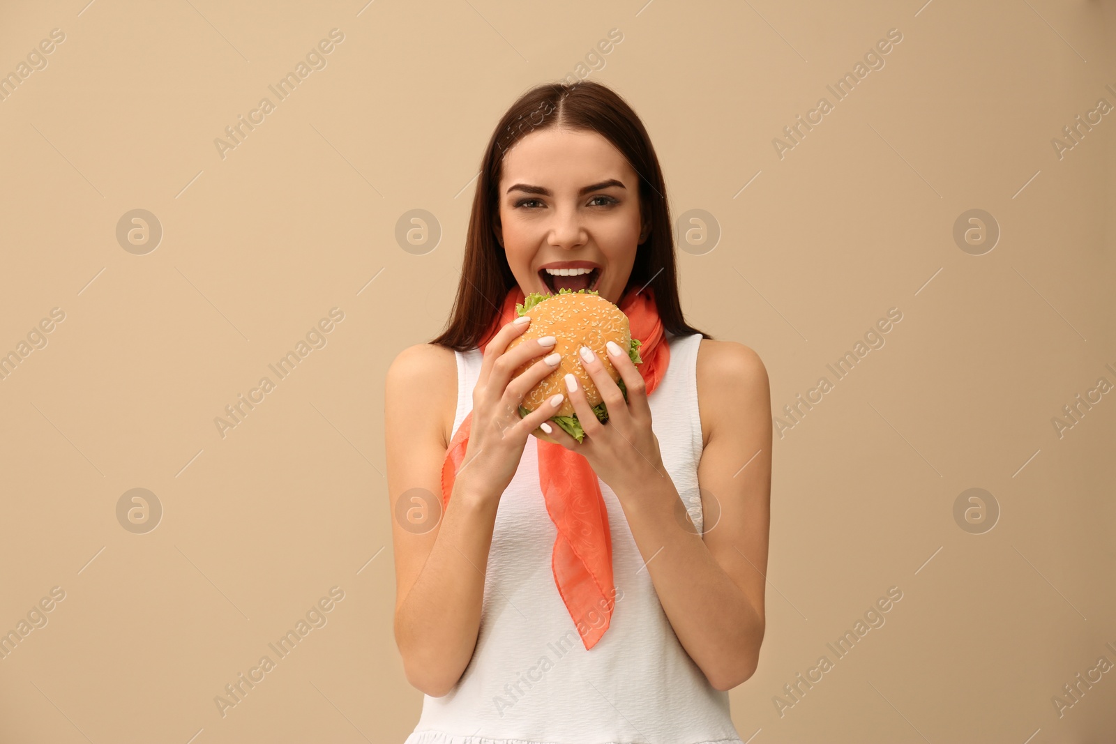 Photo of Young woman eating tasty burger on color background