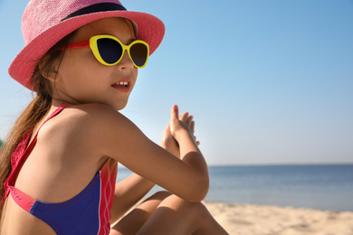 Photo of Cute little child sitting at sandy beach on sunny day