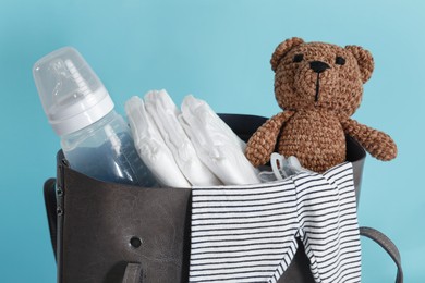 Photo of Mother's bag with baby's stuff on light blue background, closeup