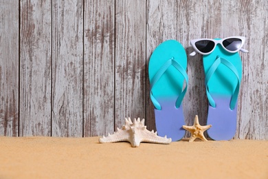 Bright flip flops and sunglasses on sand near wooden wall, space for text. Summer beach accessories