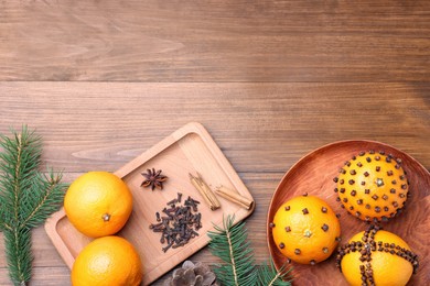 Pomander balls made of tangerines with cloves and fir branches on wooden table, flat lay. Space for text