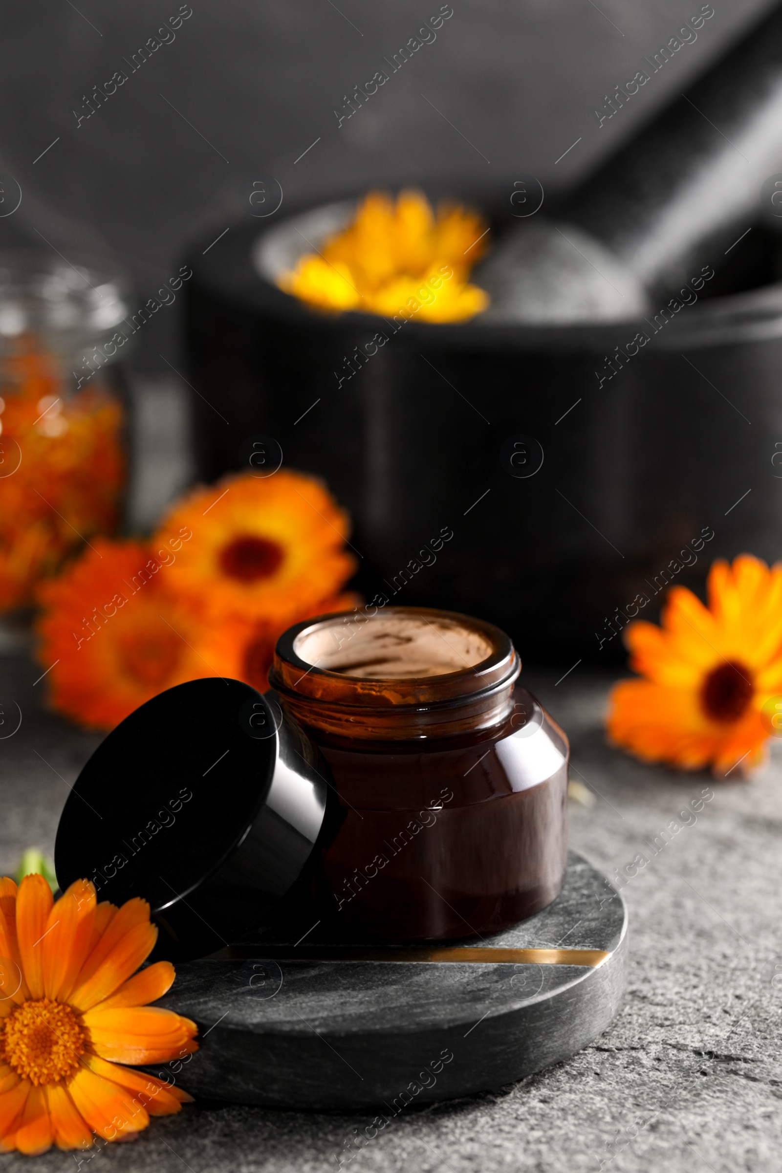 Photo of Jar of cream and beautiful calendula flowers on grey table