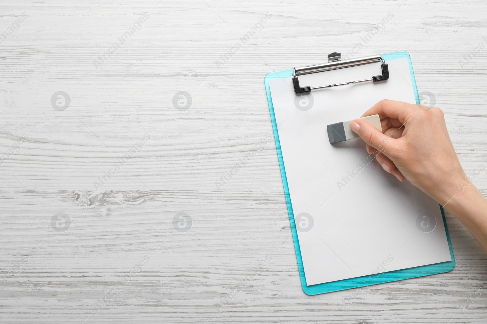 Photo of Woman erasing something on paper at white wooden table, closeup. Space for text