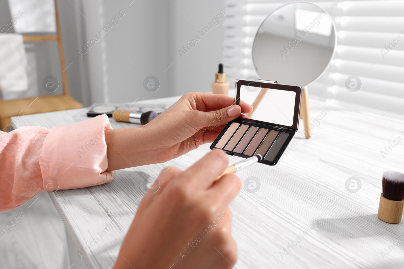 Photo of Woman with eyeshadow palette and brush at dressing table indoors, closeup