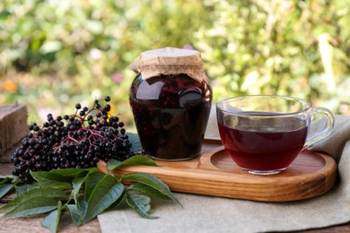 Elderberry jam, glass cup of tea and Sambucus berries on table outdoors