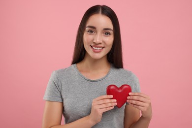 Happy young woman holding decorative red heart on pink background