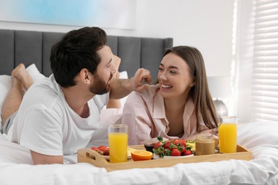 Photo of Happy couple eating tasty breakfast on bed at home